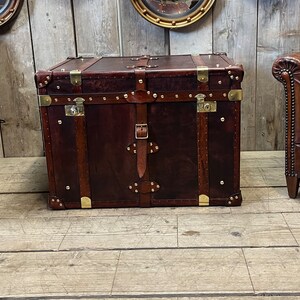 Full-grain hand dyed leather steamer trunk with hinged lift-up lid, brass stud edging and buckled straps, made in England