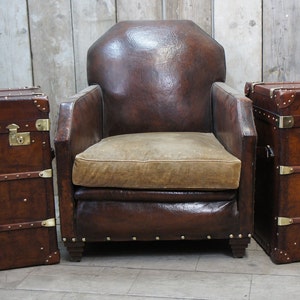 Puede incluir: Un sillón de cuero marrón con un cojín beige se encuentra entre dos baúles de cuero marrón con detalles en latón.