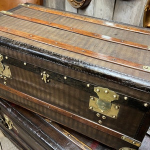 Puede incluir: Dos ba&uacute;les antiguos apilados. Los ba&uacute;les son marrones con herrajes de lat&oacute;n y listones de madera. Los ba&uacute;les tienen un patr&oacute;n de rayas y probablemente est&aacute;n hechos de cuero o un material similar. Son de principios del siglo XX.