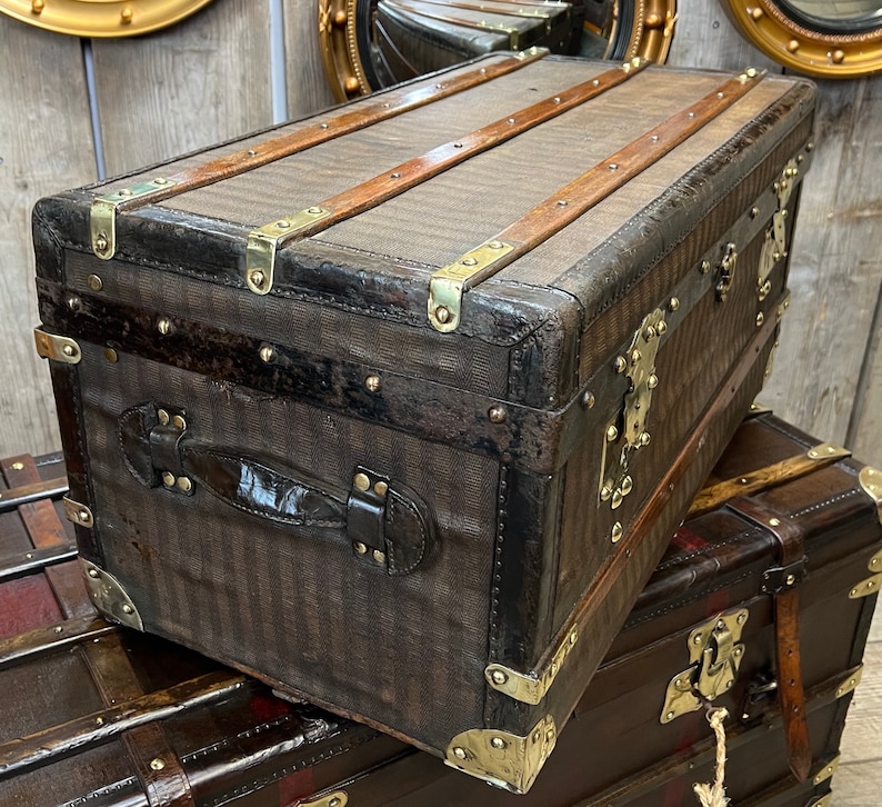 Puede incluir: Un ba&uacute;l marr&oacute;n vintage con herrajes de lat&oacute;n y detalles de cuero. El ba&uacute;l presenta un patr&oacute;n de rayas en el exterior y listones de madera en la parte superior. El ba&uacute;l rectangular tiene un asa en el lateral.
