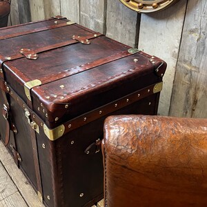 Handmade in England leather steamer trunk with full brass fittings, stud edging and leather straps on a polished white floor