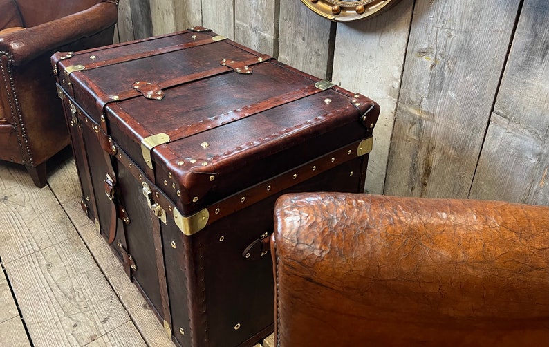 Handmade in England leather steamer trunk with full brass fittings, stud edging and leather straps on a polished white floor