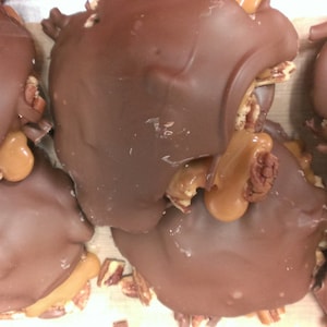 May include: Close-up of several chocolate-covered pecan pralines with caramel filling. The pralines are arranged in a pile on a white surface.