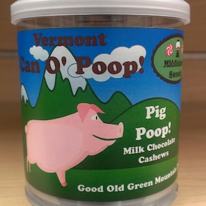 May include: A clear plastic container with a white lid filled with milk chocolate cashews. The container has a green, blue, and white label with the text "Vermont Can O' Poop! Pig Poop! Milk Chocolate Cashews Good Old Green Mountain Sweets".