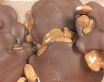 May include: Close-up of chocolate covered caramel and almonds. The caramel is a light brown color and the almonds are a light tan color. The chocolate is a dark brown color and is smooth and shiny.