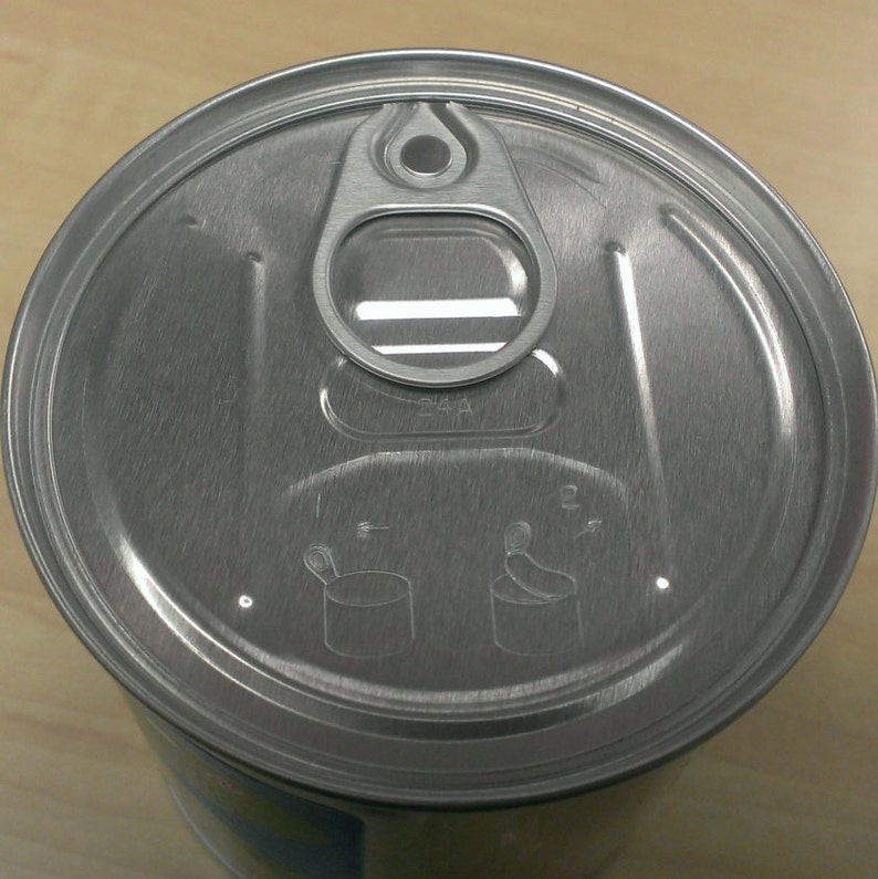 May include: A silver can lid with a pull tab and instructions for opening. The instructions show a spoon and a can with an arrow pointing to the side.
