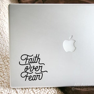 May include: A white laptop with a black sticker that says "Faith over Fear". The laptop has a silver Apple logo.