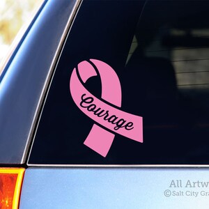 Photo of pink vinyl decal of an awareness ribbon with the word Courage cut out of front shown on SUV window