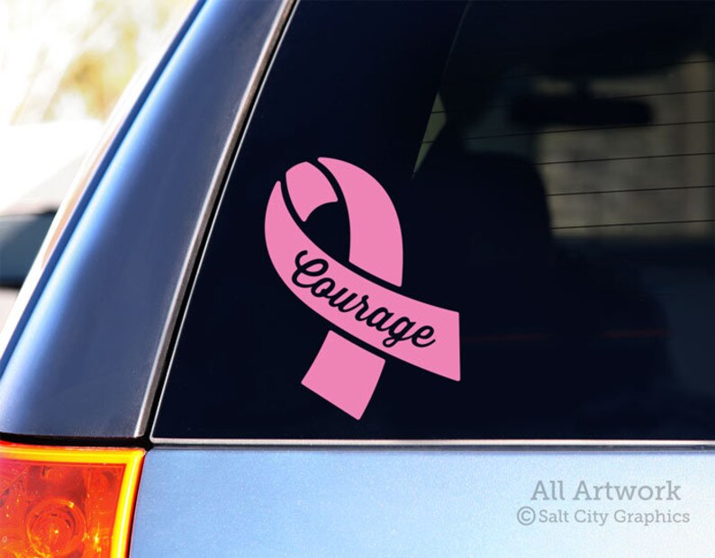 Photo of pink vinyl decal of an awareness ribbon with the word Courage cut out of front shown on SUV window