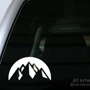 May include: White vinyl decal of a mountain range silhouette on a black background. The decal is applied to the back window of a car. The text "All Artwork © Salt City Graphics" is visible in the lower right corner of the image.