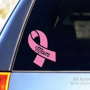 Photo of pink vinyl decal of an awareness ribbon with the word Mom cut out of front shown on SUV window