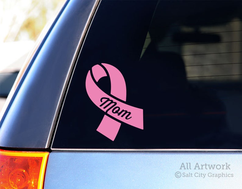Photo of pink vinyl decal of an awareness ribbon with the word Mom cut out of front shown on SUV window