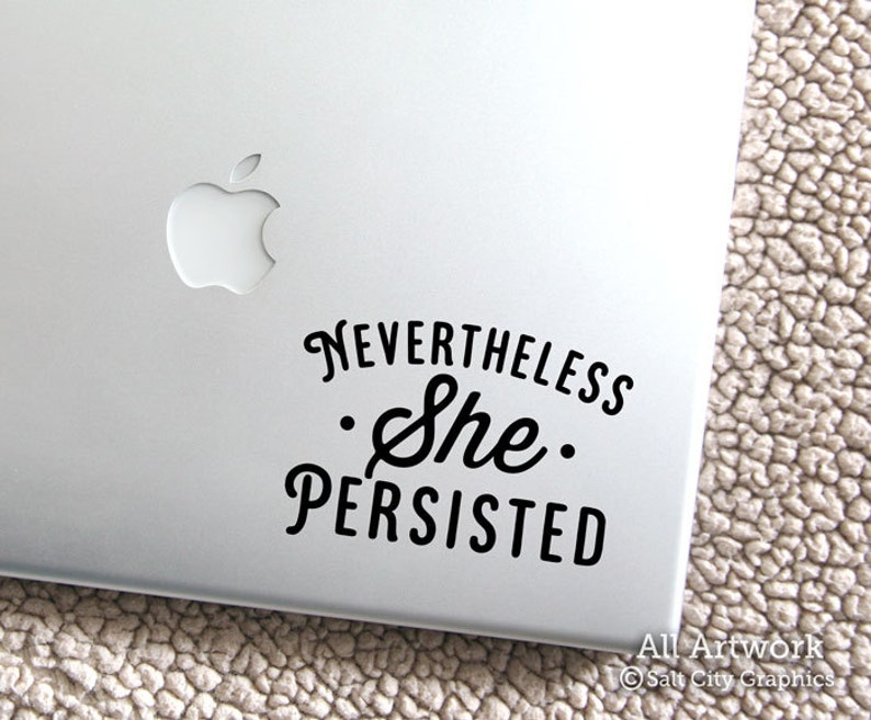 Photo of black vinyl decal of the popular phrase Nevertheless She Persisted shown on laptop