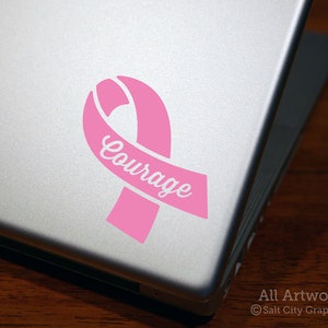 Photo of pink vinyl decal of an awareness ribbon with the word Courage cut out of front shown on laptop