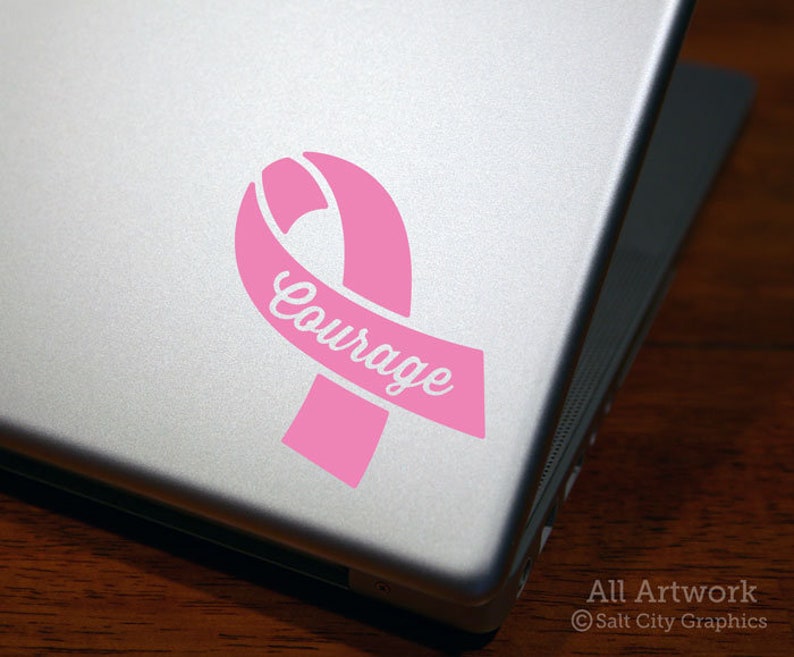Photo of pink vinyl decal of an awareness ribbon with the word Courage cut out of front shown on laptop