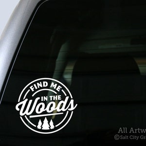 May include: White vinyl decal with the text "Find Me In The Woods" in a circle with three stylized pine trees. The decal is on a black car window.