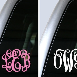 May include: Two car window decals featuring custom monograms. One is a pink, swirly monogram with the letters LCB. The other is a white, swirly monogram with the letters OWG. Both are displayed on a car window.