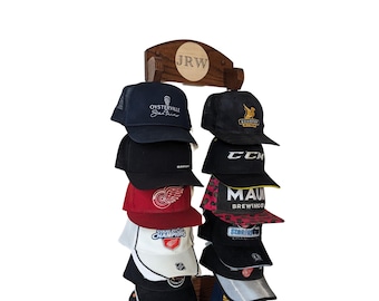 May include: A wooden hat rack displaying a collection of baseball caps. The rack is made of dark wood and features the initials "JRW" engraved on a circular plaque. The caps are in various colors and designs, including logos and text.