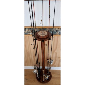 May include: A wooden fishing rod rack with a circular base and multiple slots for holding fishing rods. The base has a decorative design of a fish. The rack is made of dark wood and has a natural finish.