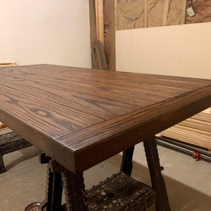 Puede incluir: Una tapa de mesa de madera marr&oacute;n oscuro con un borde grueso biselado. La tapa de la mesa est&aacute; hecha de varias tablas de madera que se han unido. La veta de la madera es visible y la tapa de la mesa tiene un acabado liso y pulido.