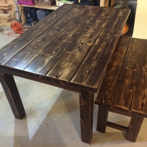 Puede incluir: Una mesa de madera marr&oacute;n oscuro con un banco a juego. La mesa tiene una tapa rectangular y cuatro patas. El banco tiene una tapa rectangular y dos patas.