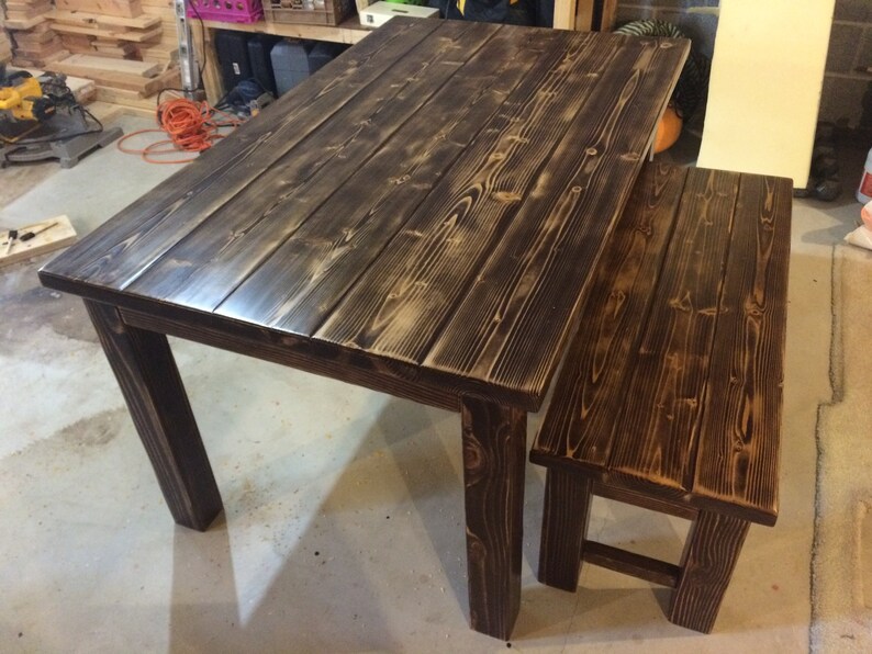 Puede incluir: Una mesa de madera marr&oacute;n oscuro con un banco a juego. La mesa tiene una tapa rectangular y cuatro patas. El banco tiene una tapa rectangular y dos patas.