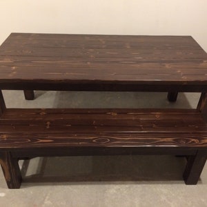 Puede incluir: Una mesa de madera marr&oacute;n oscuro con un banco a juego. La mesa tiene un estilo r&uacute;stico, de granja y est&aacute; hecha de madera maciza.
