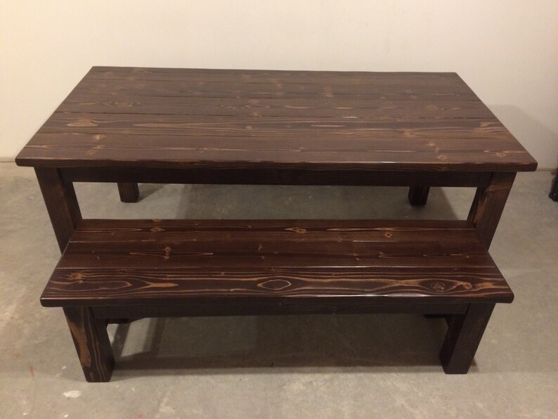 Puede incluir: Una mesa de madera marr&oacute;n oscuro con un banco a juego. La mesa tiene un estilo r&uacute;stico, de granja y est&aacute; hecha de madera maciza.