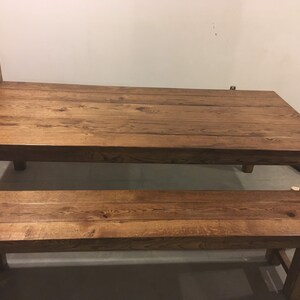 Puede incluir: Un conjunto de mesa y banco de madera r&uacute;stica con un tinte marr&oacute;n oscuro. La mesa tiene una tapa rectangular y cuatro patas. El banco tiene una tapa larga y rectangular y cuatro patas.