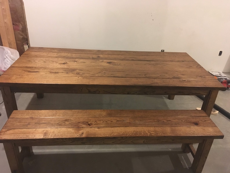 Puede incluir: Un conjunto de mesa y banco de madera r&uacute;stica con un tinte marr&oacute;n oscuro. La mesa tiene una tapa rectangular y cuatro patas. El banco tiene una tapa larga y rectangular y cuatro patas.