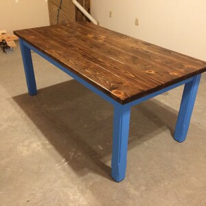 Puede incluir: Una mesa de madera con una tapa te&ntilde;ida de color marr&oacute;n oscuro y patas pintadas de azul. La mesa est&aacute; hecha de madera maciza y tiene un aspecto r&uacute;stico.