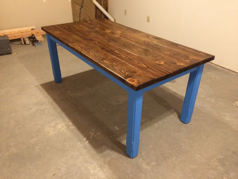 Puede incluir: Una mesa de madera con una tapa te&ntilde;ida de color marr&oacute;n oscuro y patas pintadas de azul. La mesa est&aacute; hecha de madera maciza y tiene un aspecto r&uacute;stico.