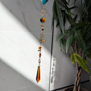 May include: A gold-toned crystal suncatcher with a honeycomb design, a bee, and amber-colored beads. The suncatcher is hanging from a gold chain.