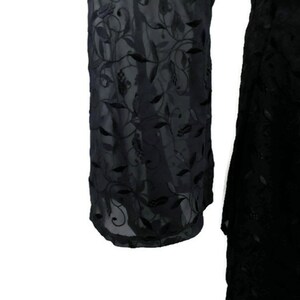 Pode incluir: Vestido preto transparente com um padr&atilde;o de bordado floral. O vestido tem mangas compridas e uma saia fluida.