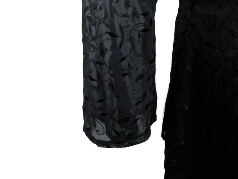 Pode incluir: Vestido preto transparente com um padr&atilde;o de bordado floral. O vestido tem mangas compridas e uma saia fluida.