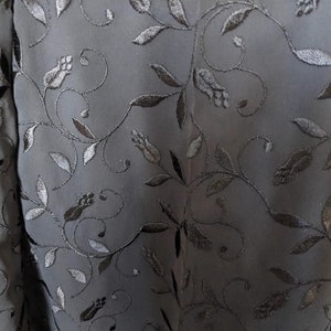 Pode incluir: Tecido preto com um delicado padr&atilde;o floral bordado em fio preto. O padr&atilde;o apresenta pequenas folhas e flores.