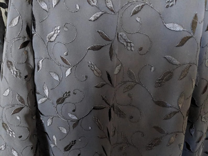 Pode incluir: Tecido preto com um delicado padr&atilde;o floral bordado em fio preto. O padr&atilde;o apresenta pequenas folhas e flores.