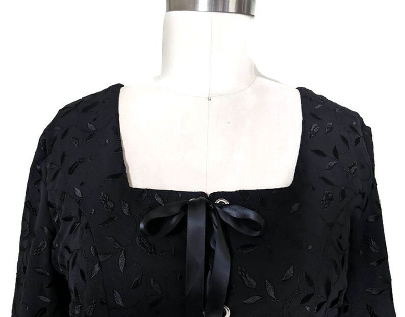 Pode incluir: Top preto de manga curta com decote quadrado e detalhe de renda na frente. O top &eacute; feito de um tecido macio e texturizado com um padr&atilde;o floral.