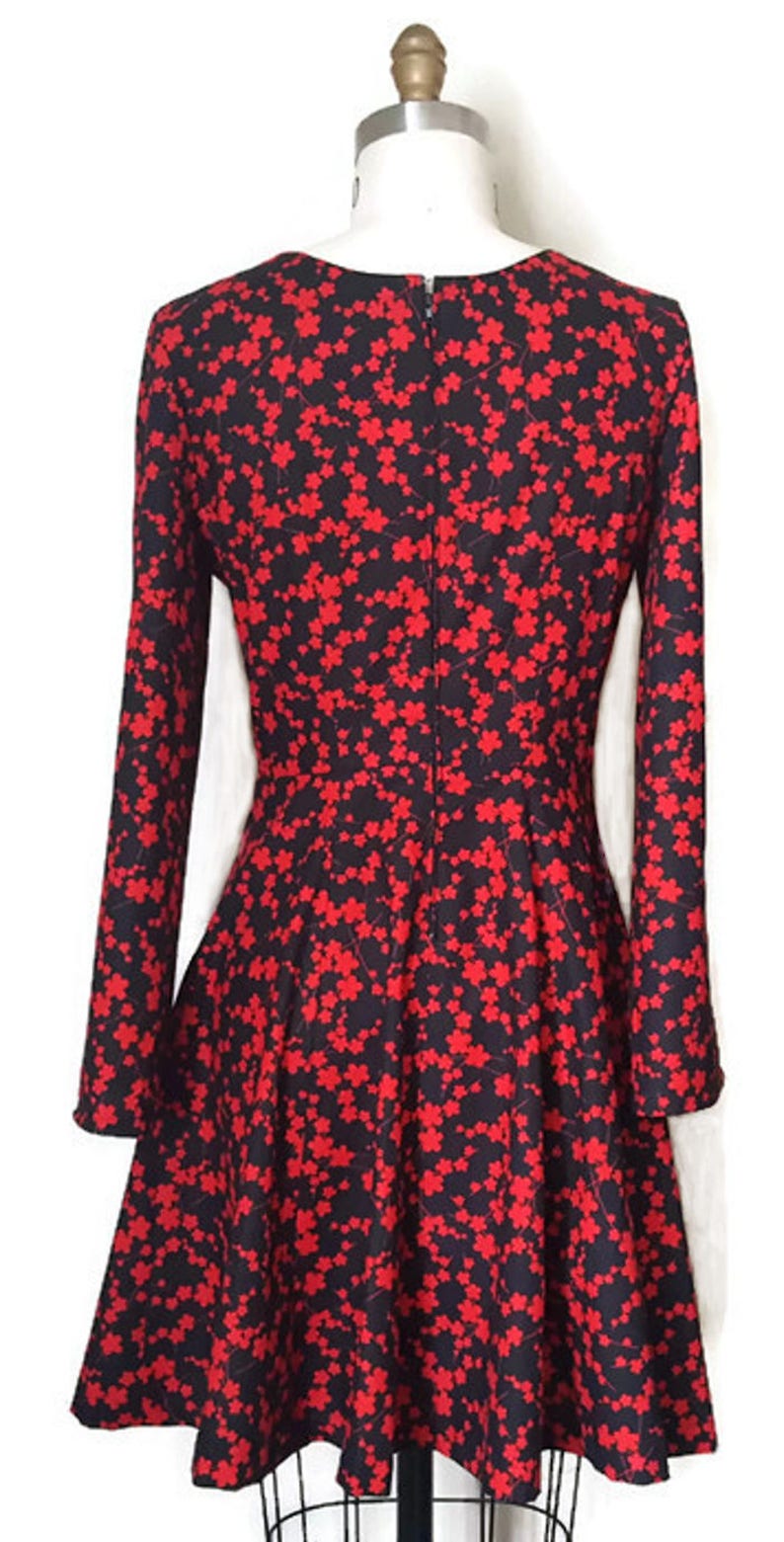 K&ouml;nnte beinhalten: Ein schwarzes und rotes Kleid mit Blumenmuster. Das Kleid hat lange &Auml;rmel und einen taillierten Oberteil. Der Rock ist ausgestellter und reicht bis knapp &uuml;ber das Knie.