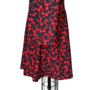 K&ouml;nnte beinhalten: Ein schwarzes Kleid mit rotem Blumendruck und einem mehrlagigen Rock. Das Kleid hat ein figurbetontes Oberteil und einen flie&szlig;enden Rock.