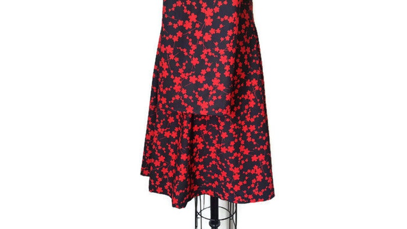 K&ouml;nnte beinhalten: Ein schwarzes Kleid mit rotem Blumendruck und einem mehrlagigen Rock. Das Kleid hat ein figurbetontes Oberteil und einen flie&szlig;enden Rock.