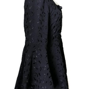 Pode incluir: Vestido preto com padr&atilde;o de folhas e mangas compridas. O vestido tem um decote quadrado e um la&ccedil;o na frente.