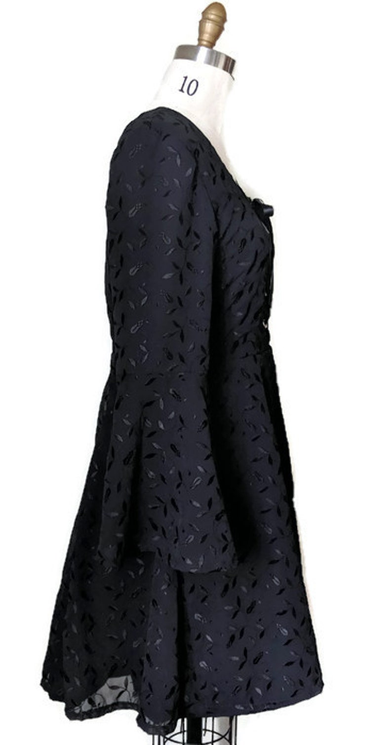 Pode incluir: Vestido preto com padr&atilde;o de folhas e mangas compridas. O vestido tem um decote quadrado e um la&ccedil;o na frente.