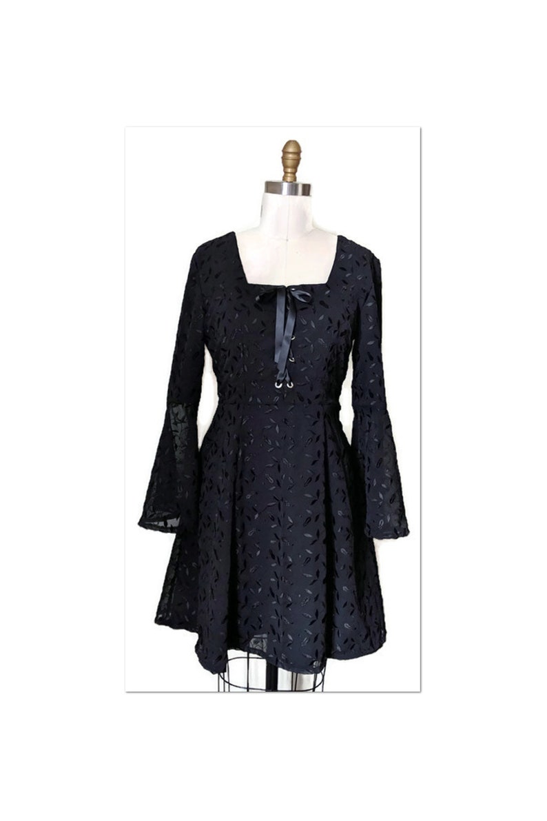 Pode incluir: Um vestido preto com decote quadrado e mangas compridas bufantes. O vestido tem um detalhe de la&ccedil;o na frente e &eacute; decorado com um padr&atilde;o de folhas pretas.