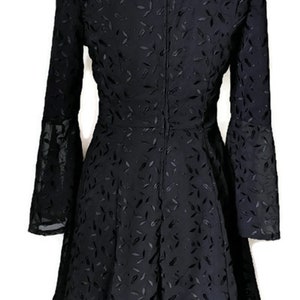 Pode incluir: Um vestido preto com padr&atilde;o de folhas e mangas compridas. O vestido tem um decote quadrado e um fecho de correr nas costas.