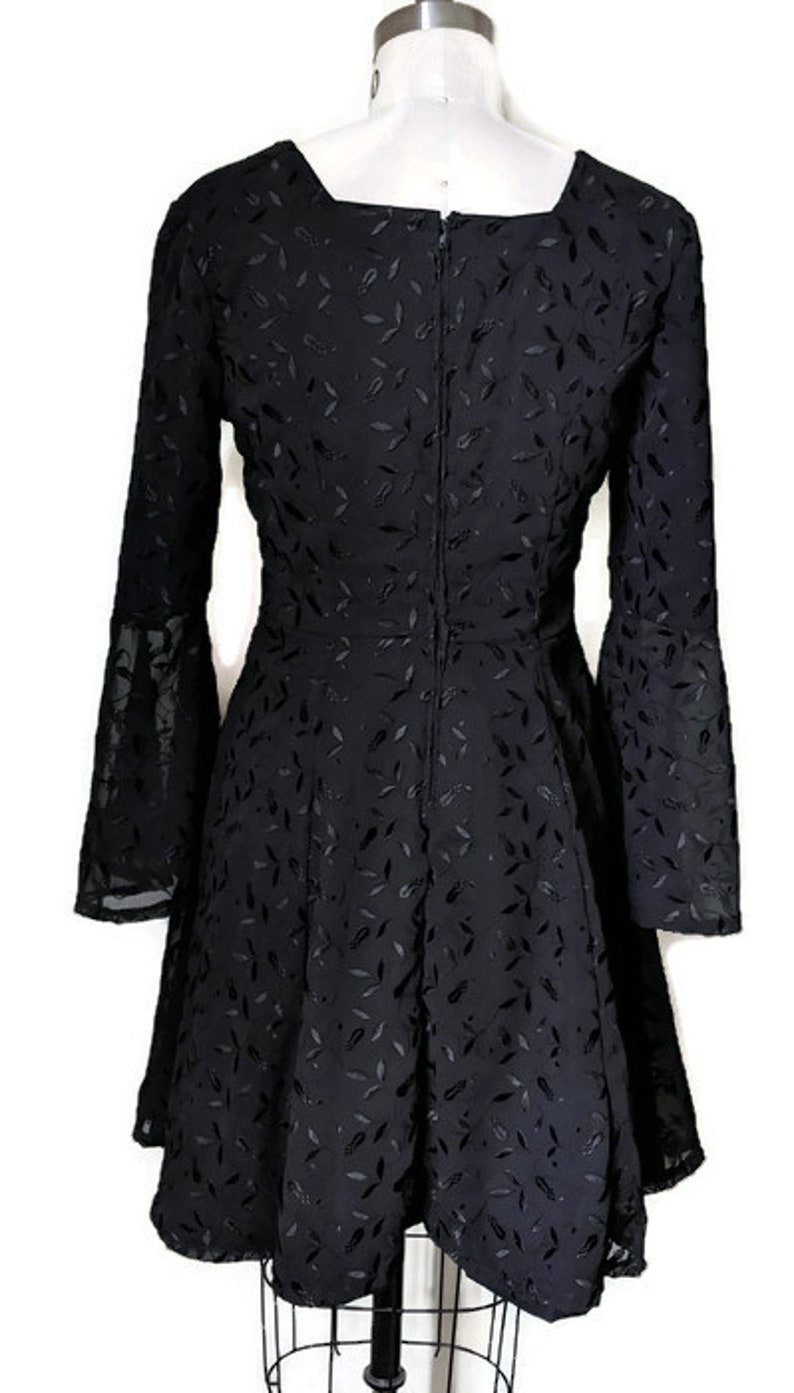 Pode incluir: Um vestido preto com padr&atilde;o de folhas e mangas compridas. O vestido tem um decote quadrado e um fecho de correr nas costas.