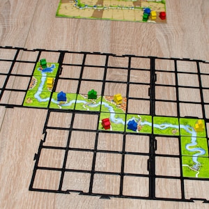 Peut inclure: Un jeu de société avec un cadre noir et une rivière verte, brune et bleue. Il y a de petites maisons jaunes, bleues, vertes et rouges.