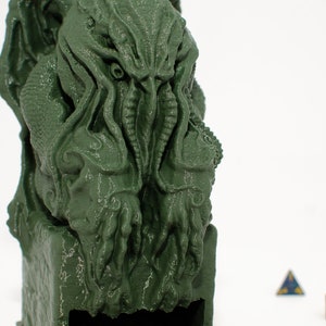 May include: Green 3D printed statue of a Cthulhu-like creature with tentacles. The statue is sitting on a base with a slot in the front.