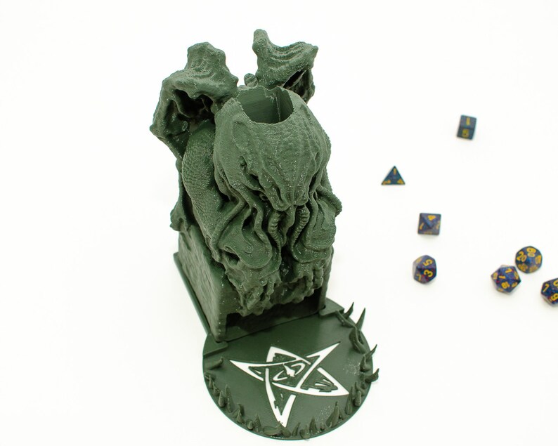 May include: Green 3D printed dice tower shaped like a Cthulhu monster with a five-pointed star base. The tower is designed to hold dice for tabletop games.