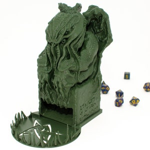 May include: Green 3D printed dice tower shaped like a Cthulhu monster with a circular base with spikes. The tower has a slot for dice to fall out of. There are several blue dice with yellow numbers on a white surface.